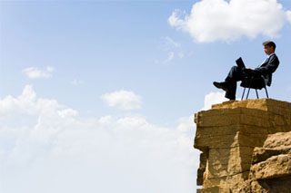 Businessman sitting on a chair at the top of a precipitous ledge.
