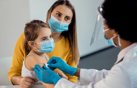 Female doctor placing adhesive bandage on little girl's arm after vaccination.