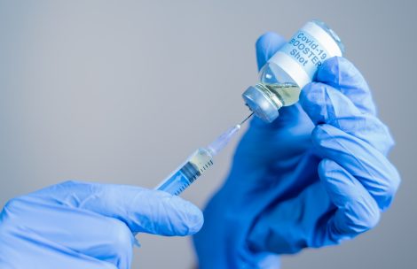 Focus on syringe, close up of doctor or nurse hands taking covid vaccination booster shot or 3rd dose from syringe.