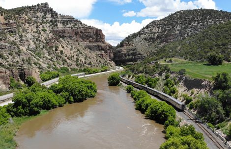 A passenger train follows the Colorado River and Interstate 70 as it winds its way through Glenwood Canyon.