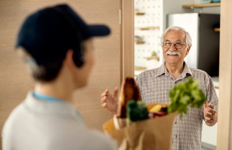 Happy senior man talking to deliverer who is brining him bag with groceries at home.