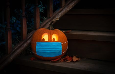 Lighted Halloween pumpkin wearing COVID mask on wooden steps.