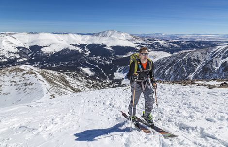 A back country skier skinning uphill while high on a mountain.