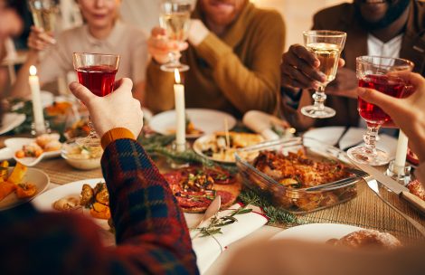 Close up of adult people raising glasses while enjoying Christmas dinner at home, copy space.