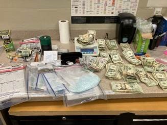 An image showing items discovered following a vehicle pursuit on Interstate 70 in Garfield County. Suspected narcotics, cash, and other assorted items are displayed on a table.