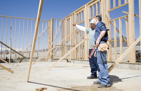 Builders on construction site with framed walls in the background.