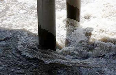 High water flows against bridge supports on the Colorado River.