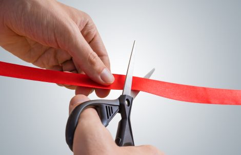 Man hands are cutting red ribbon with scissors.