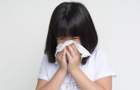 Portrait of a sick girl standing with napkin close her nose.