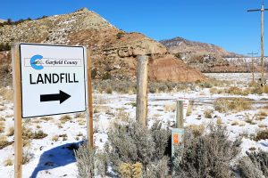 A sign reading the word landfill is seen outside the Garfield County Landfill near Rifle, Colorado. There is snow on the ground amidst the sage and mountains in the background.